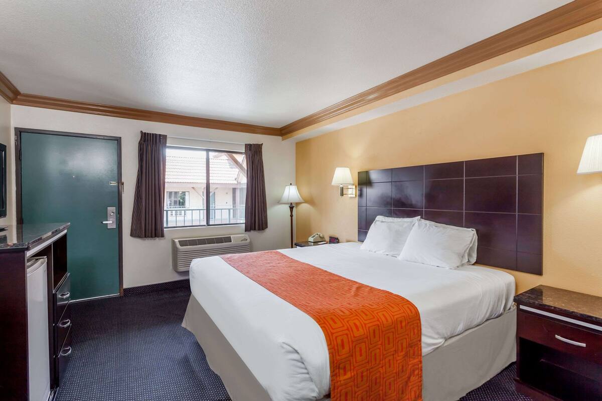 A hotel room with a large bed, a desk, a chair, a lamp, and a window with curtains.