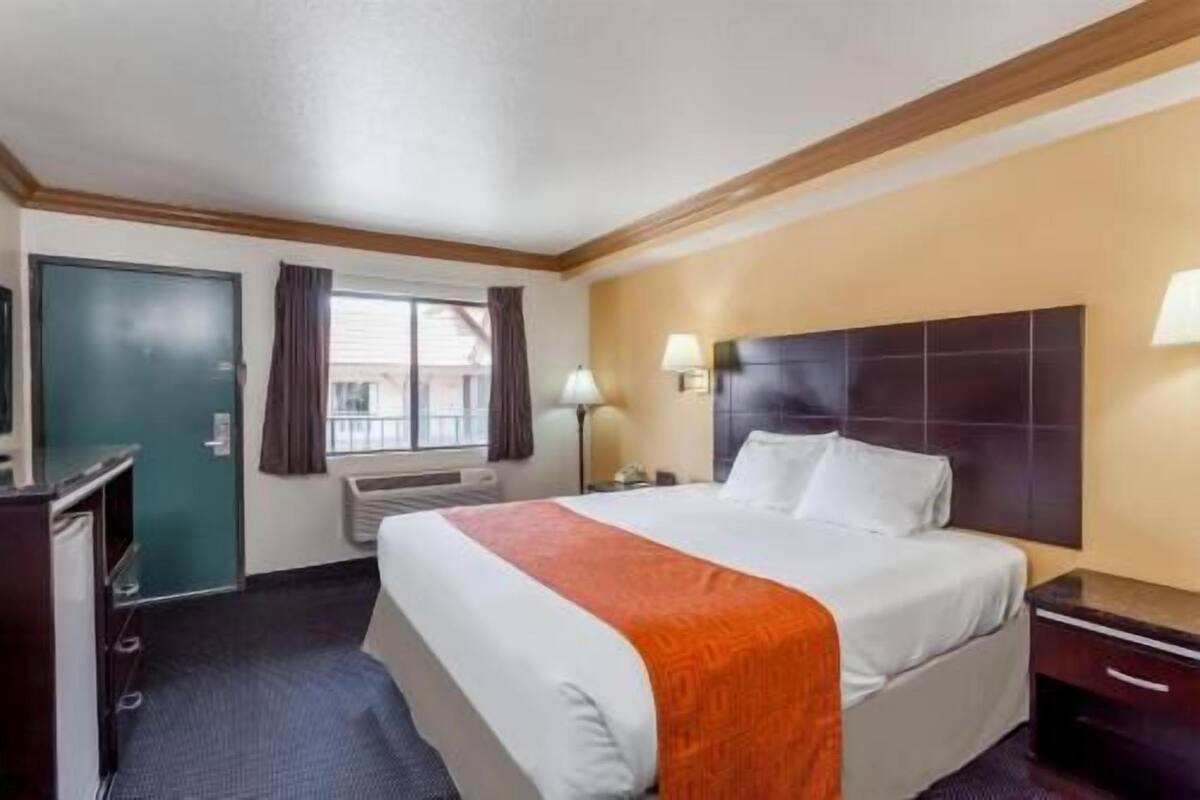 A hotel room with a bed, bedside lamps, a desk, and a window with curtains.