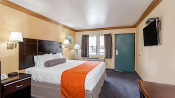 Habitación de hotel con cama, mesita de noche, lámpara y televisor montado en la pared.