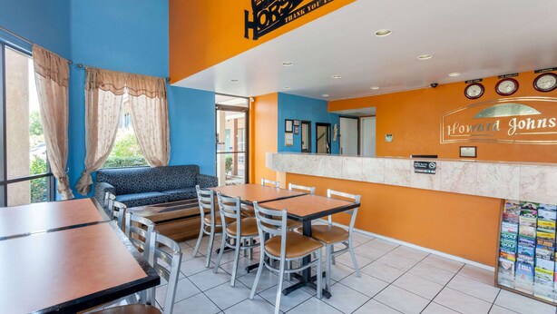 A restaurant with a blue and orange color scheme, featuring a counter with a name sign, a seating area with tables and chairs, and a view of the outdoors. - Howard Johnson by Wyndham Norco (Norco)