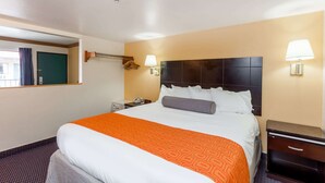 A hotel room with a large bed, a nightstand, a lamp, and a window with curtains. - Howard Johnson by Wyndham Norco (Norco)