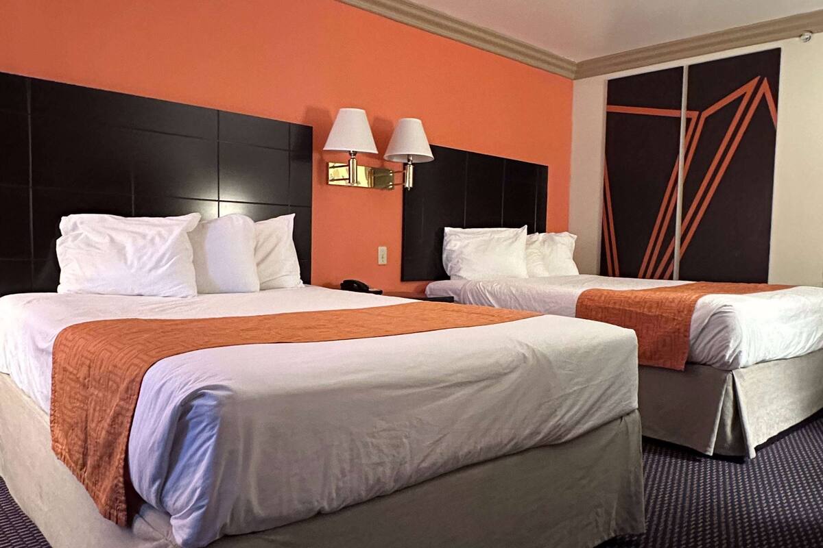 A hotel room with two beds, a black headboard, a wall-mounted lamp, and a geometric design on the wall.