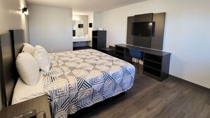 A modern hotel room with a large bed, a desk, a flat-screen TV, and a minibar.
