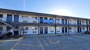 A multi-story motel with a 'NOW OPEN' sign, a handicapped parking space, and a stairway to the upper floors.