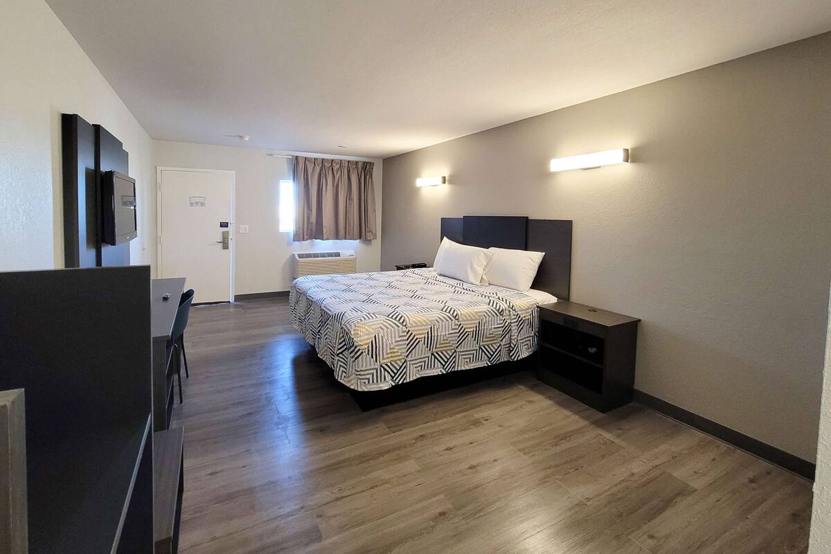 A modern hotel room with a large bed, a desk, and a television.