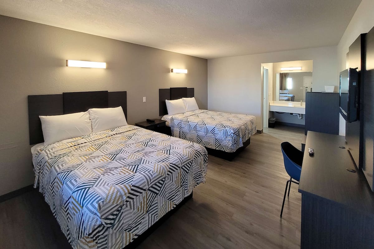 A hotel room with two beds, a desk, a chair, a TV, and a bathroom visible through an open door.
