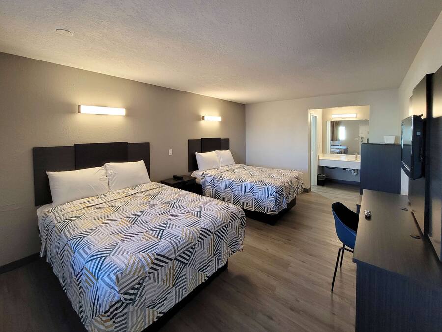 A hotel room with two beds, a desk, a chair, a TV, and a bathroom visible through an open door.
