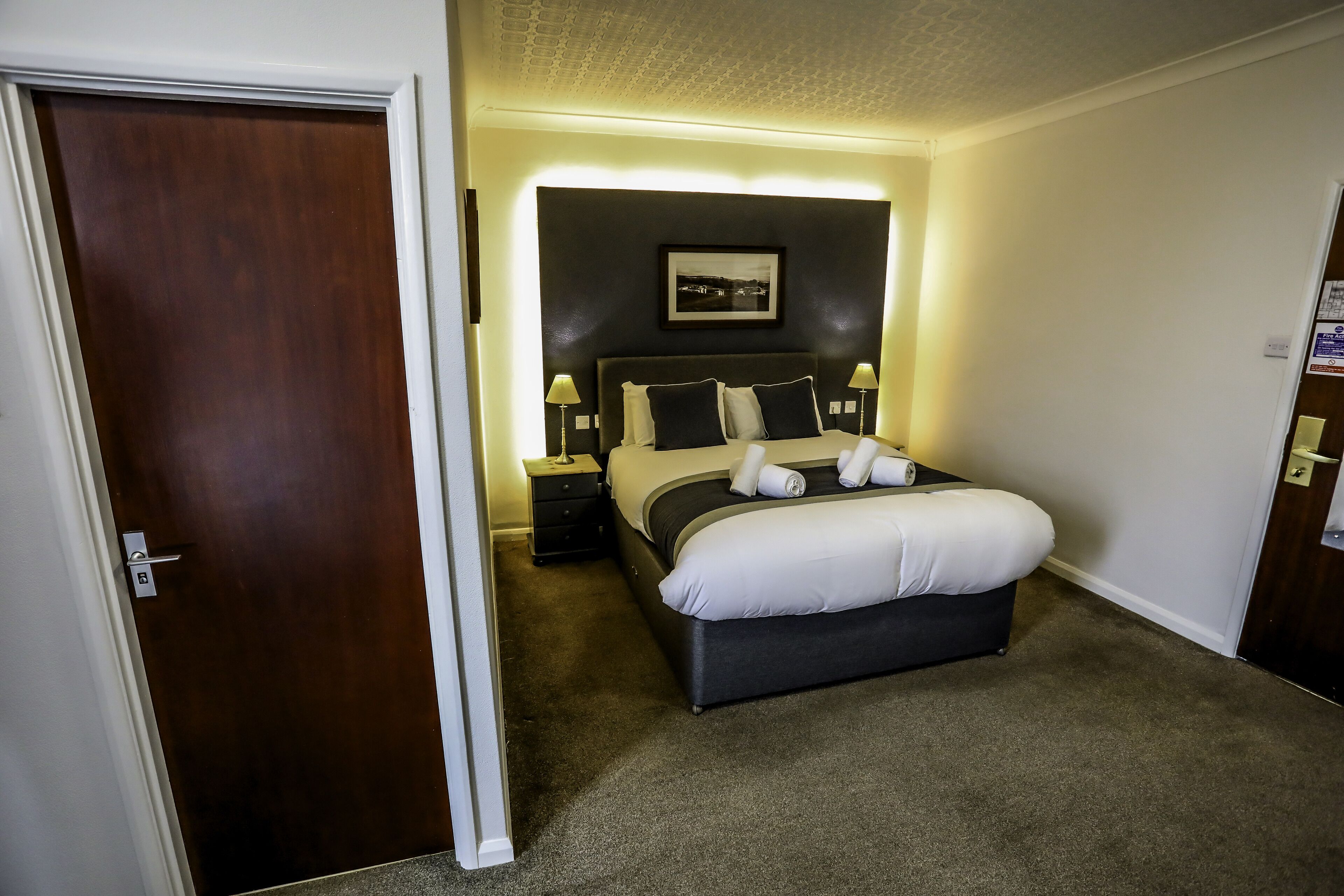 A hotel room with a bed, bedside lamps, a nightstand, and a framed picture on the wall.