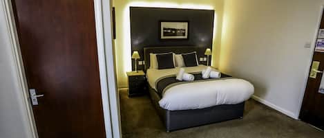 Una habitación de hotel con cama, lámparas de noche, una mesita de noche y un cuadro en la pared.