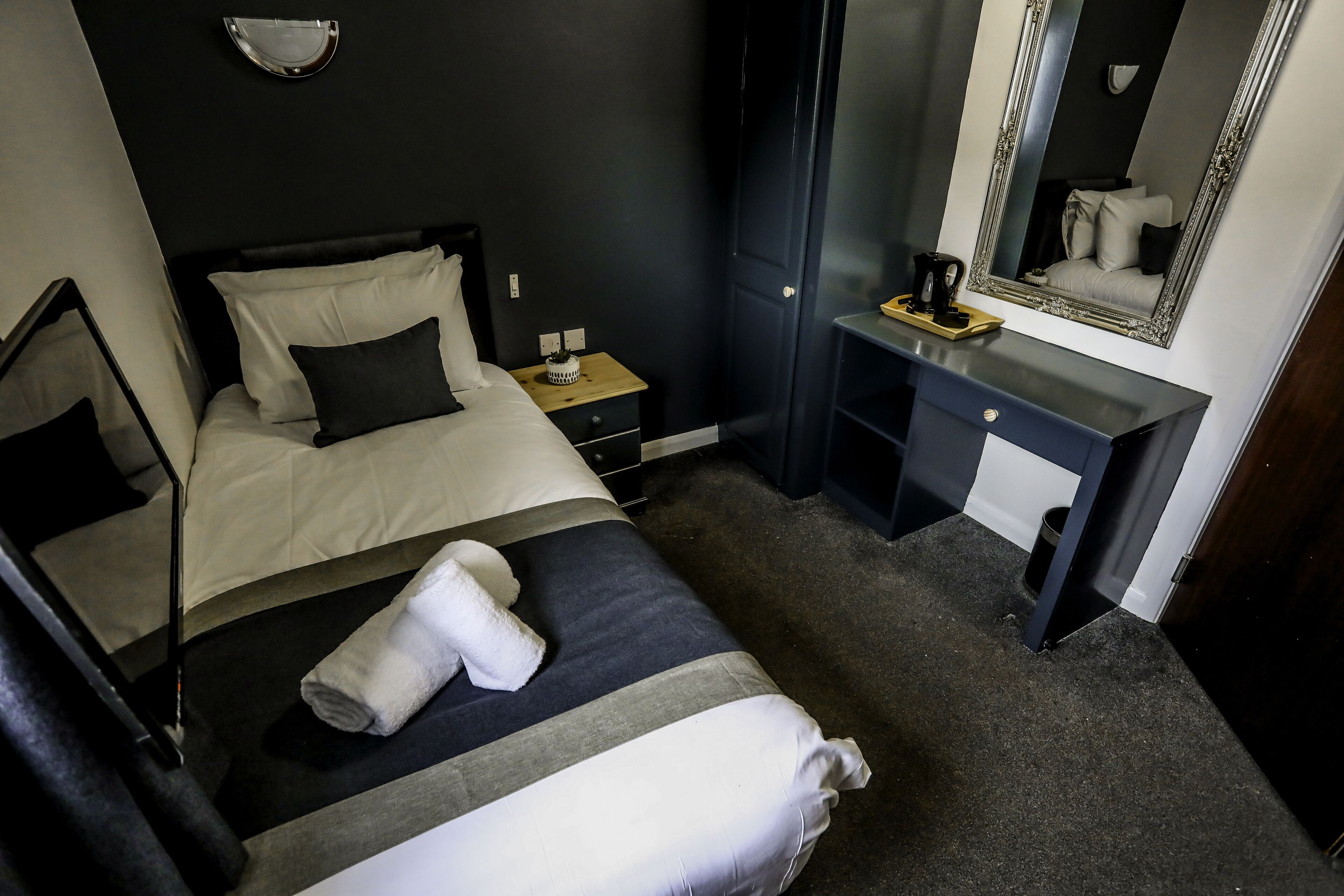 Quarto de hotel com cama, mesa de cabeceira e escrivaninha com cadeira.