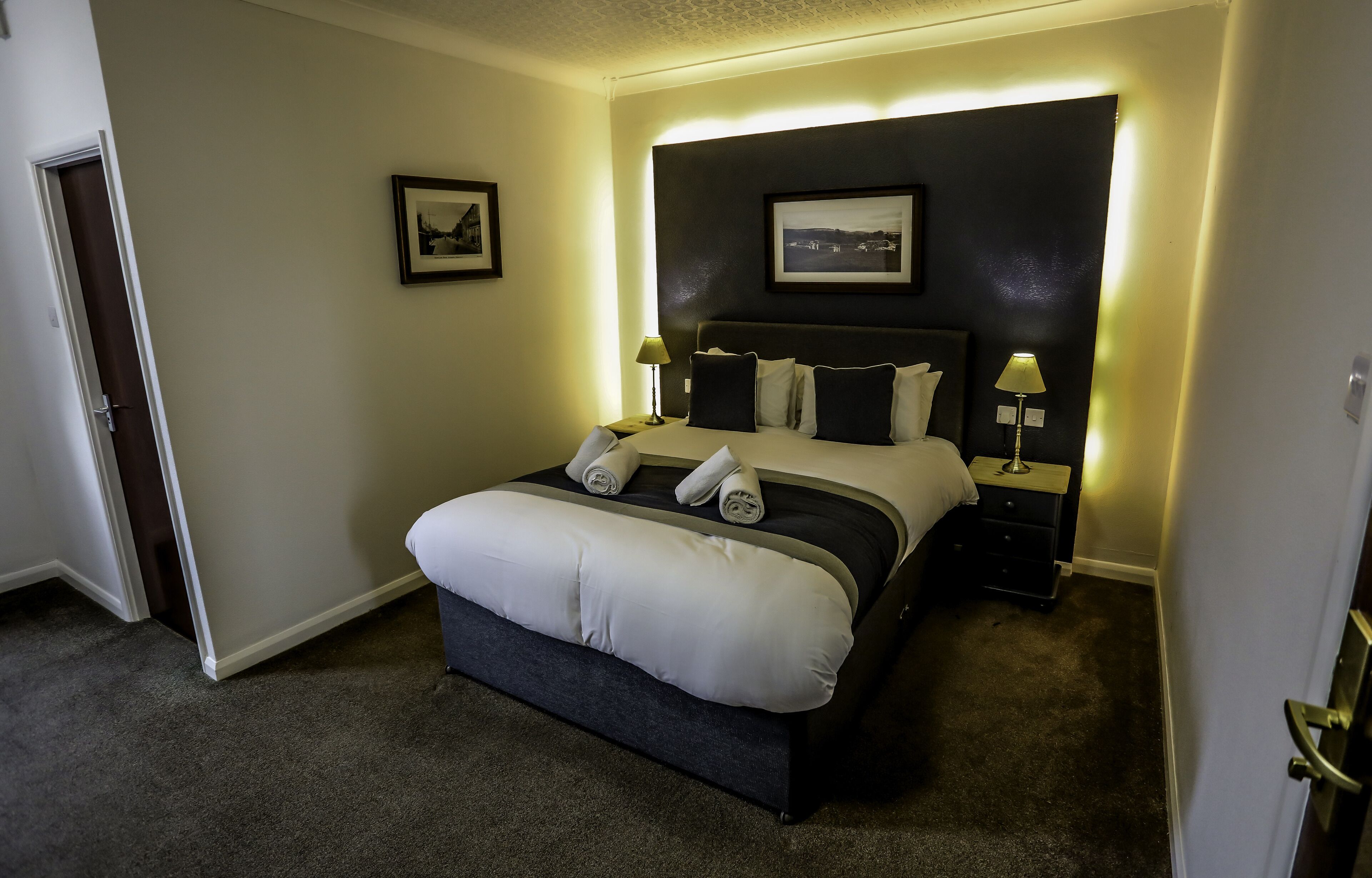 A neatly made bed with white and dark bedding, two bedside lamps, and a framed picture on the wall.