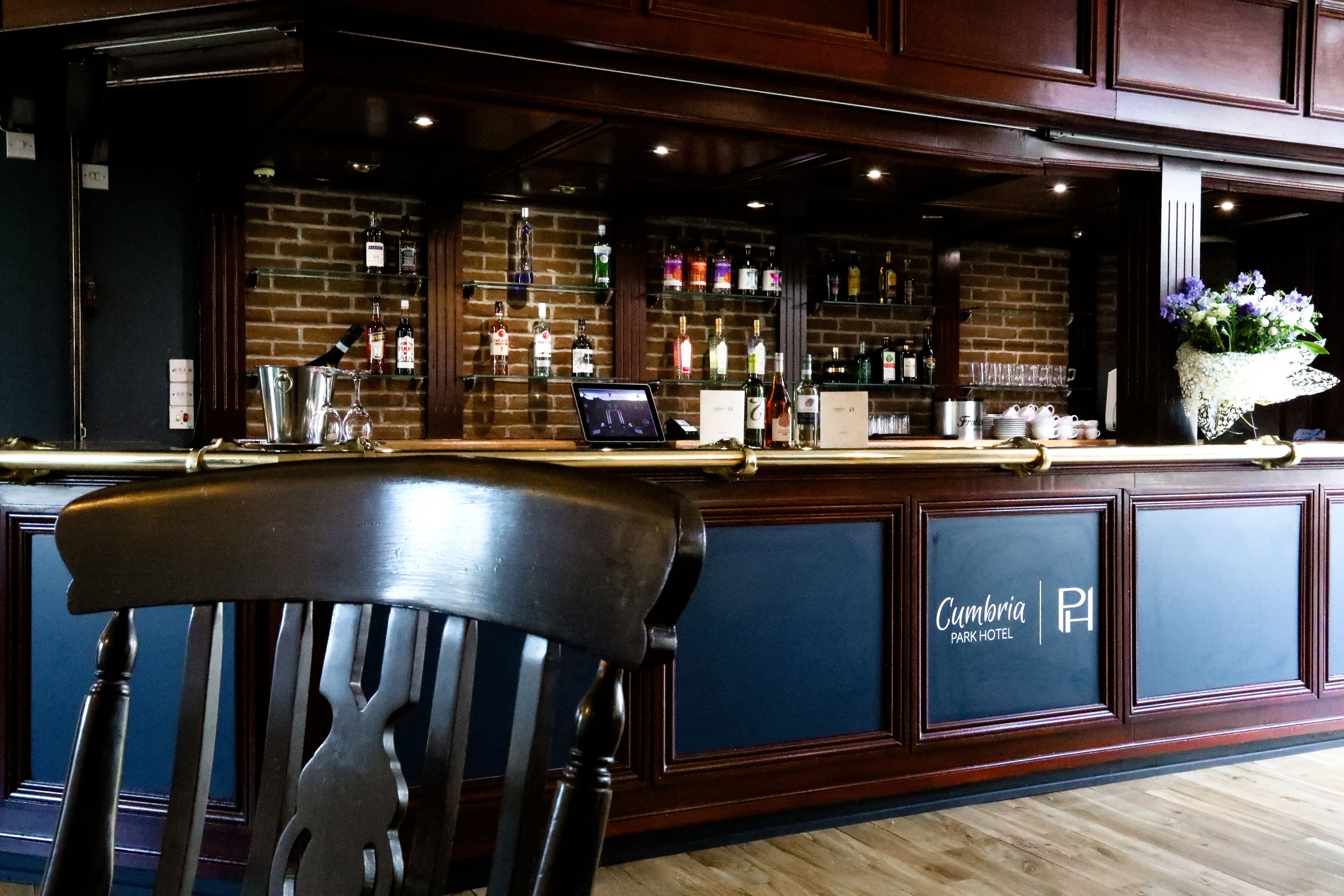 A bar area with a wooden counter, a laptop, and a variety of liquor bottles.