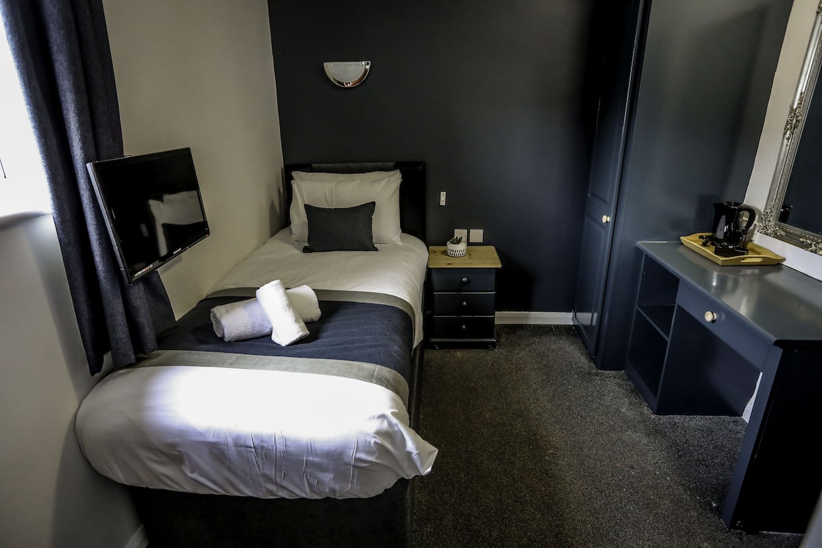A hotel room with a bed, a bedside table, a desk, a mirror, and a wall-mounted light fixture.