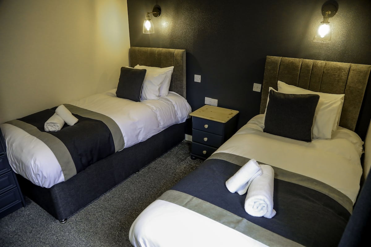 A hotel room with two beds, each with a headboard, a nightstand, and a drawer.