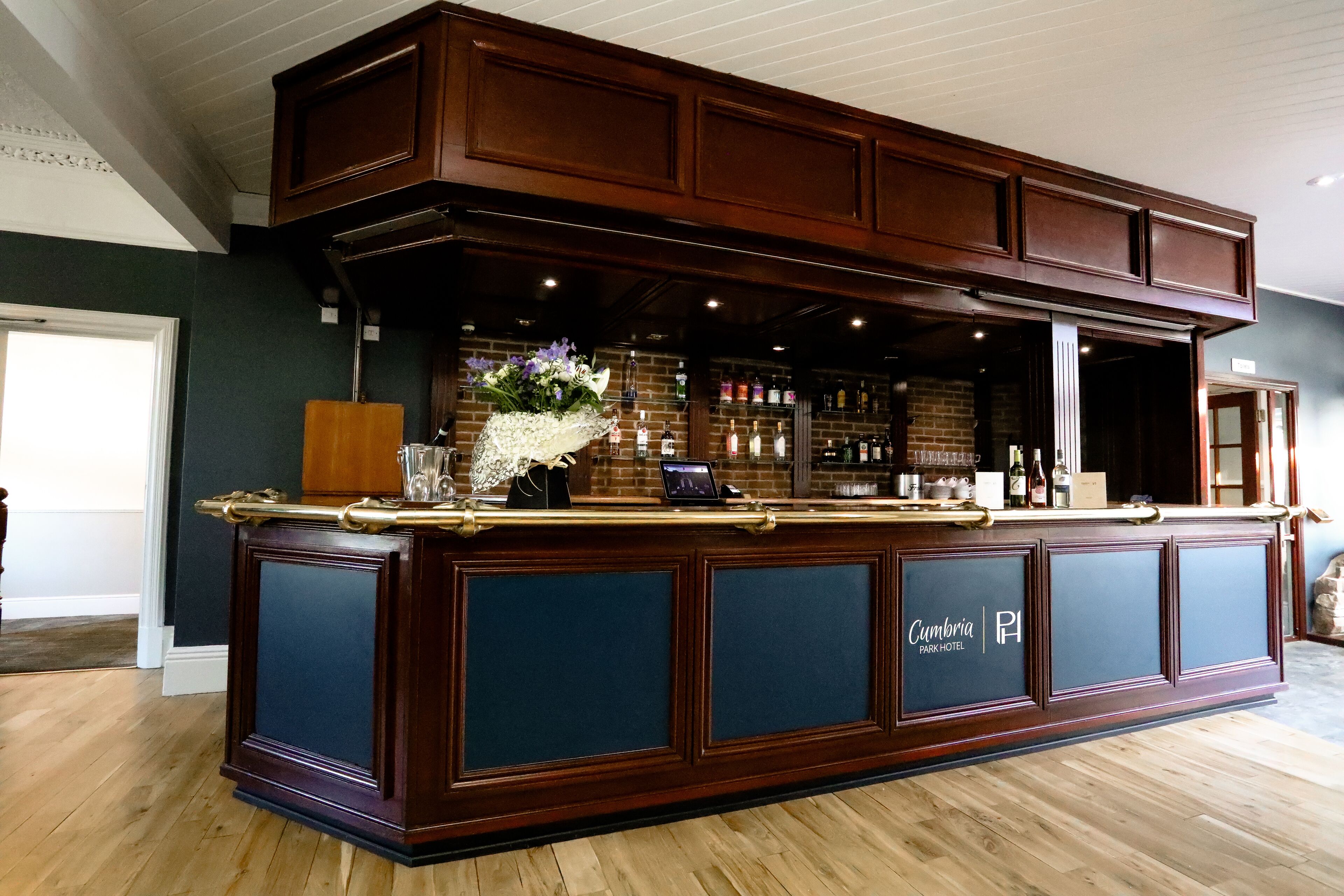 Zona de bar con detalles en madera oscura, un letrero que dice "Cumbria Park Hotel" y una variedad de bebidas embotelladas.