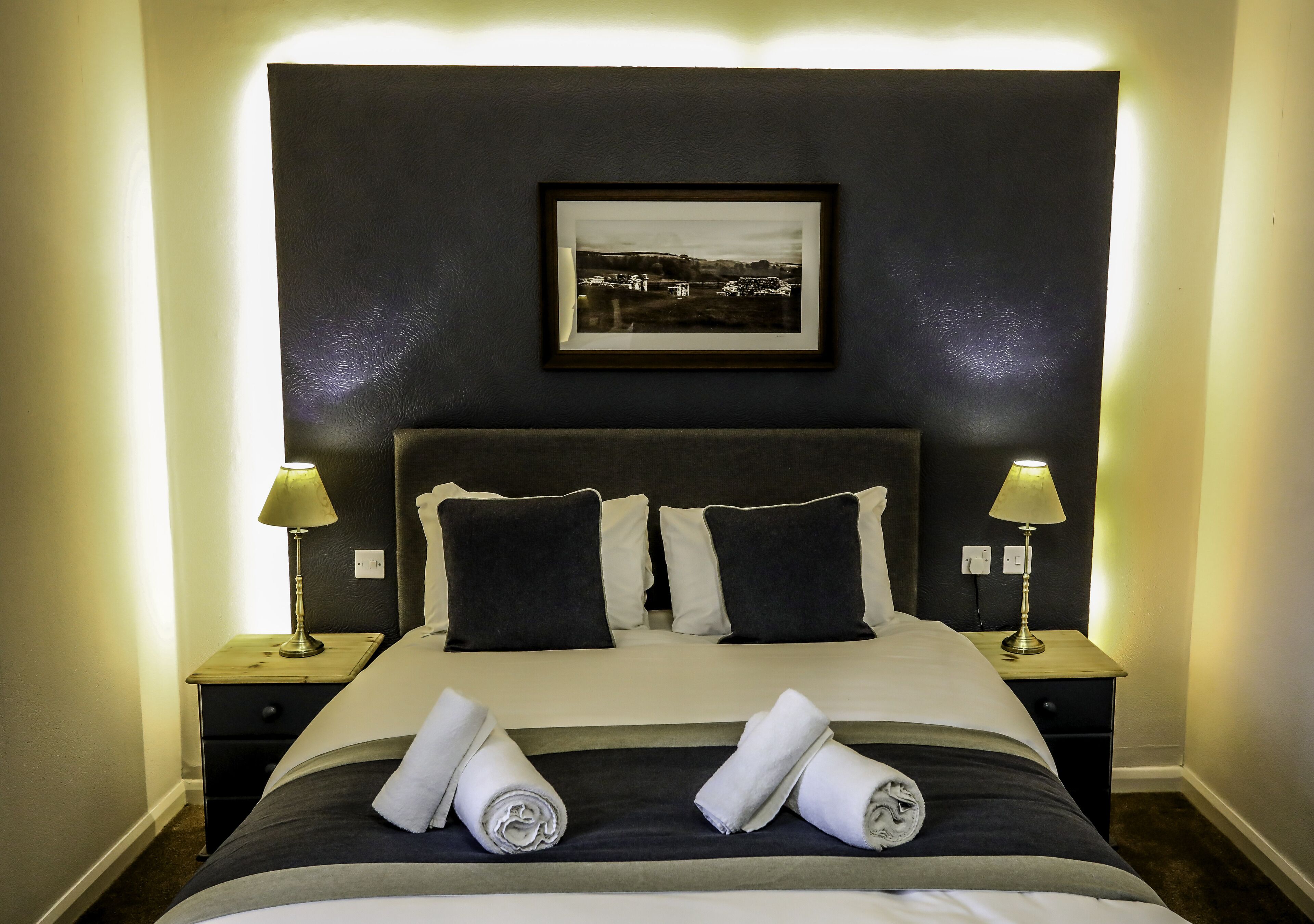 A neatly made bed with a dark headboard, two bedside lamps, and a framed picture on the wall.