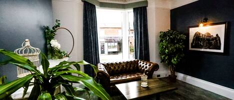 A living room with a leather sofa, a wooden coffee table, a chandelier, and a large potted plant.
