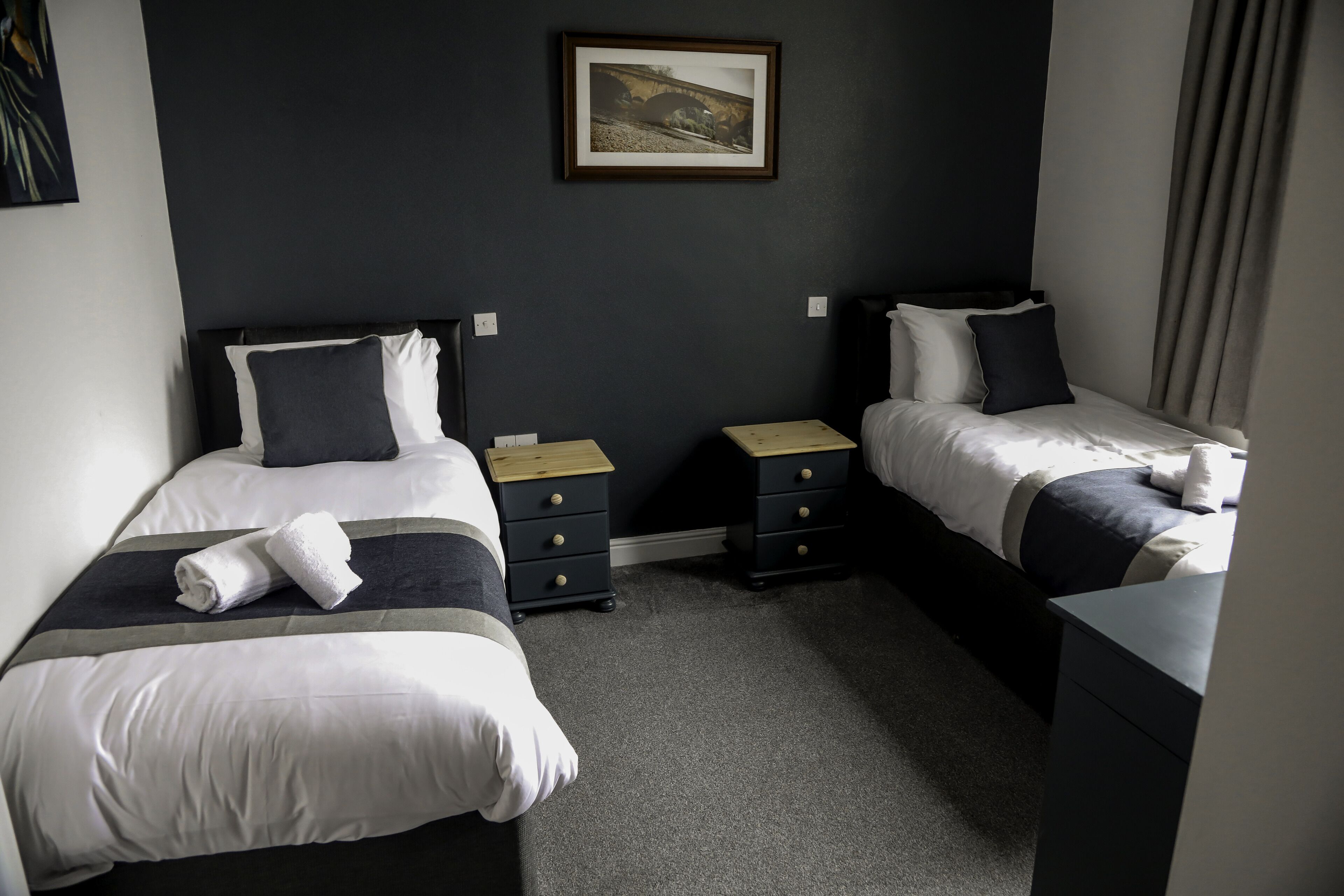 Una habitación de hotel con dos camas, paredes oscuras y un cuadro en la pared.