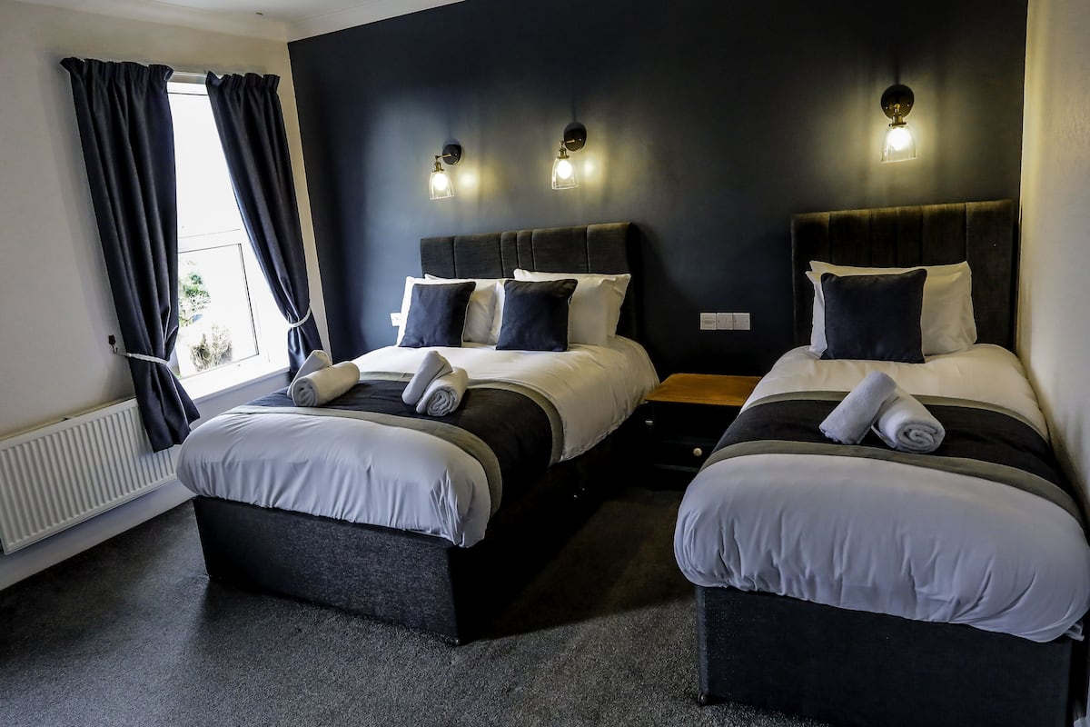 A double room with two beds, each with a headboard, a nightstand, and a window with curtains.