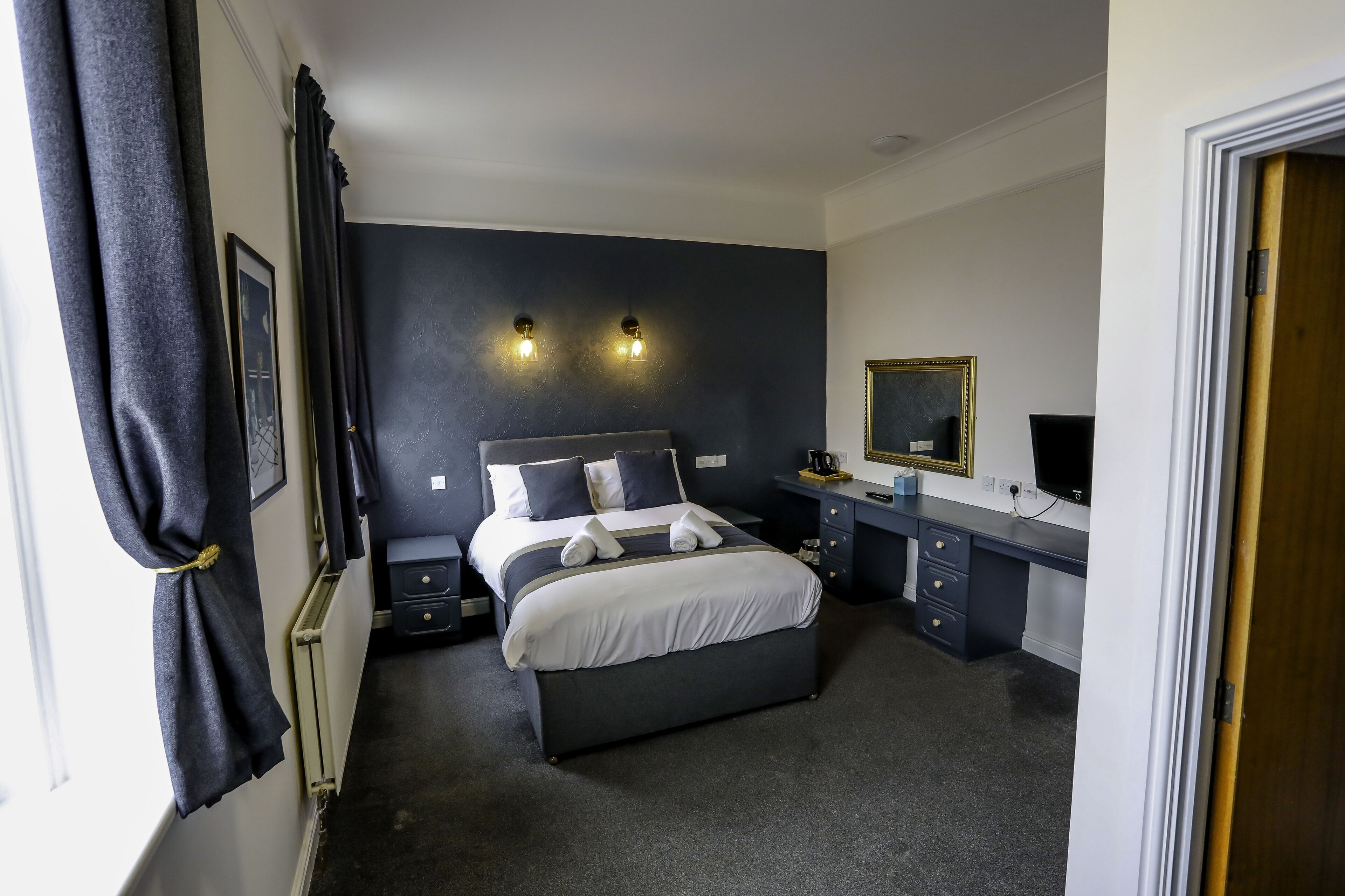 A bedroom with a large bed, bedside tables, a desk, and a mirror.