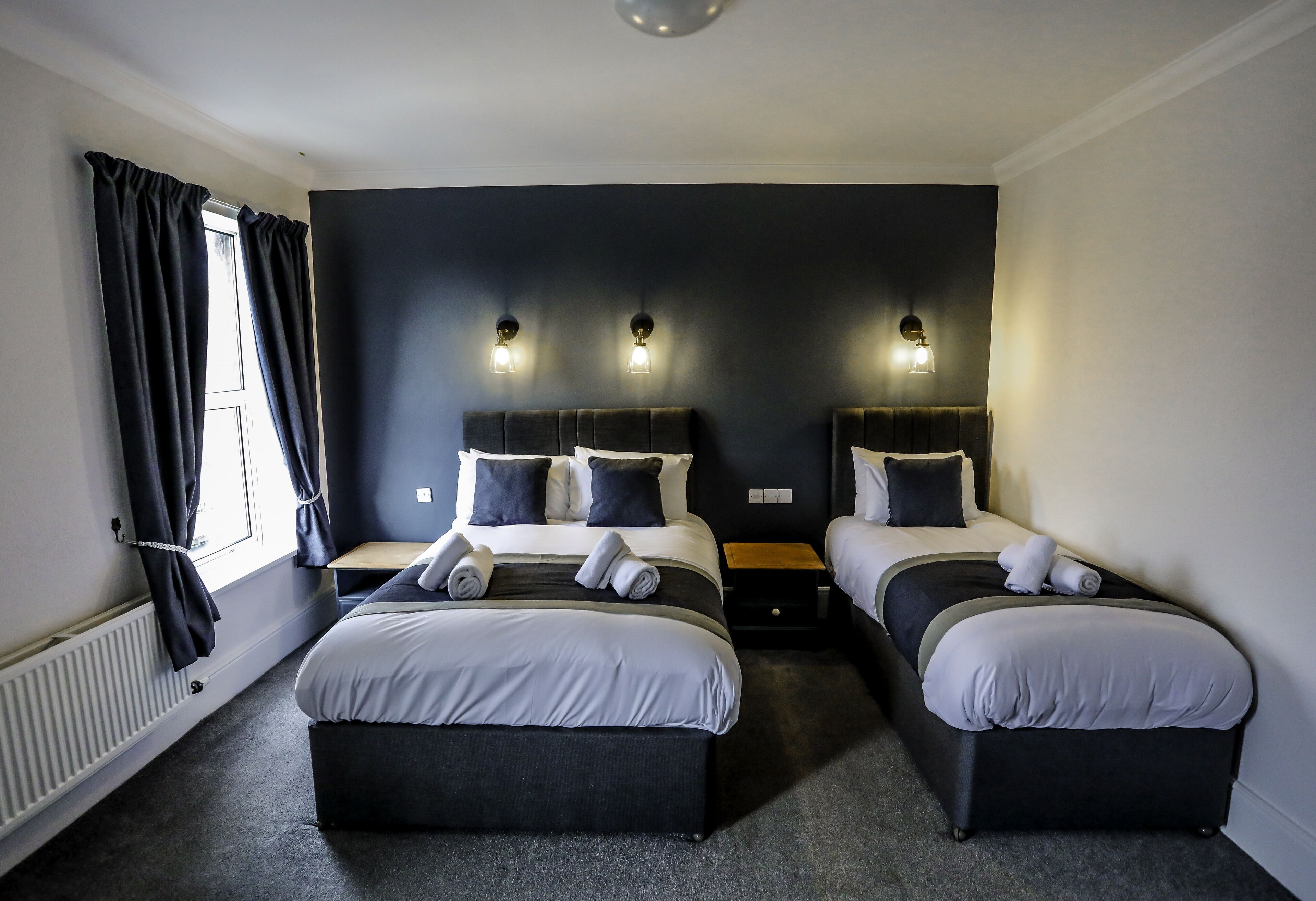 Une chambre d’hôtel avec deux lits, des murs sombres et trois lampes fixées au mur.