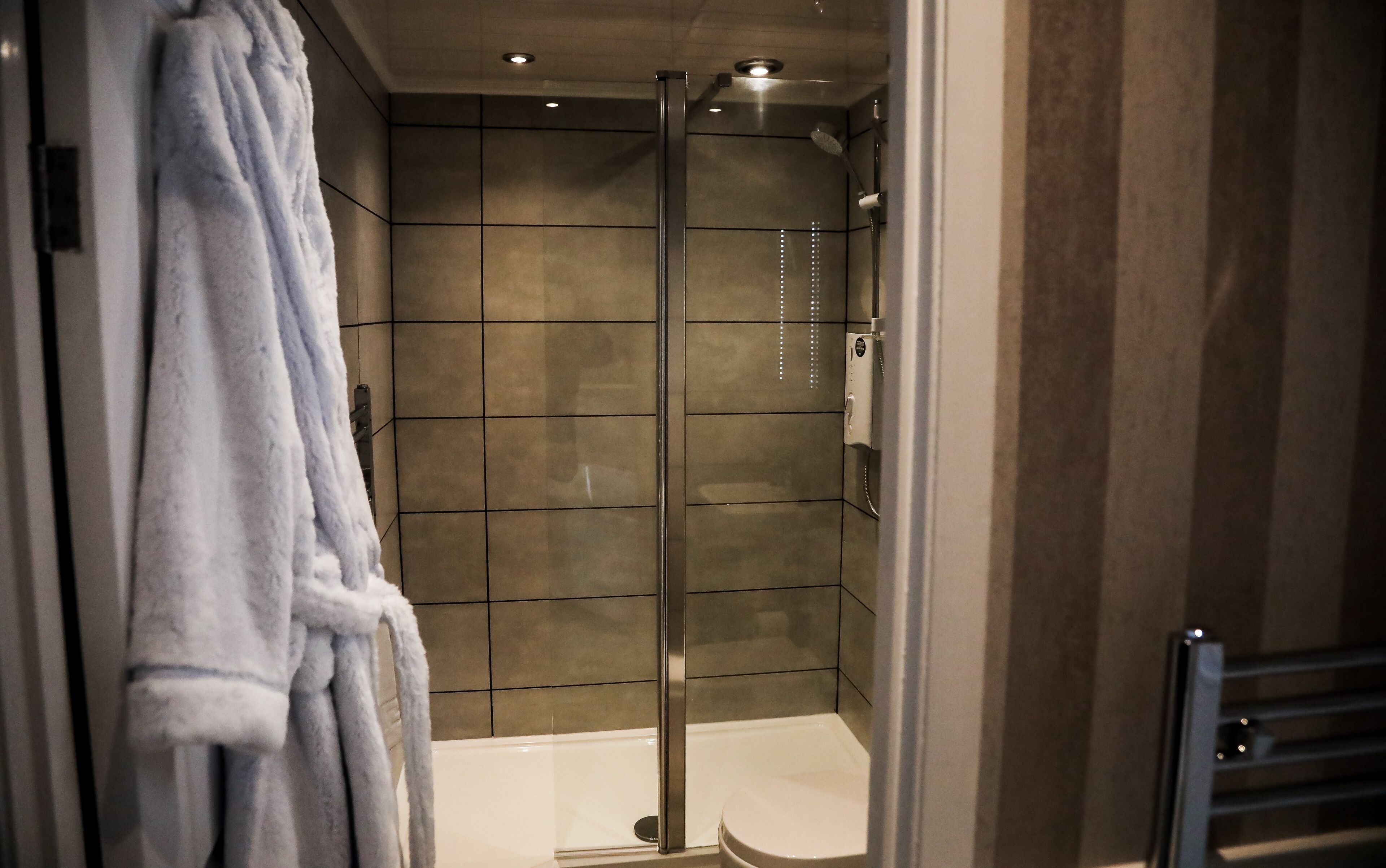 A modern bathroom with a glass shower enclosure, a white bathtub, and a towel rack.