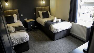 A hotel room with two beds, a small bedside table, a nightstand, and a window with a view of the street.