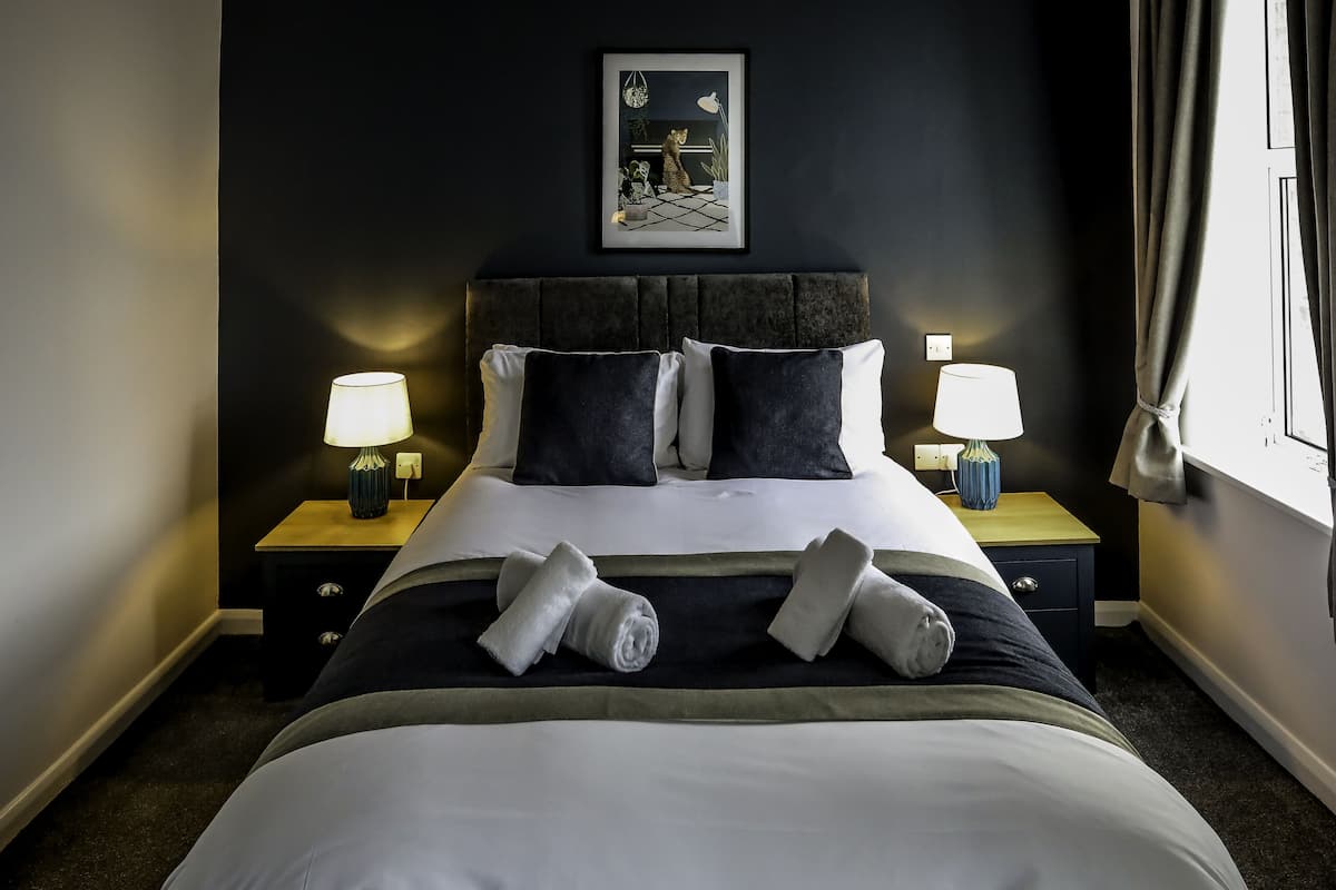 A neatly made bed with two pillows, two bedside lamps, and two rolled towels.