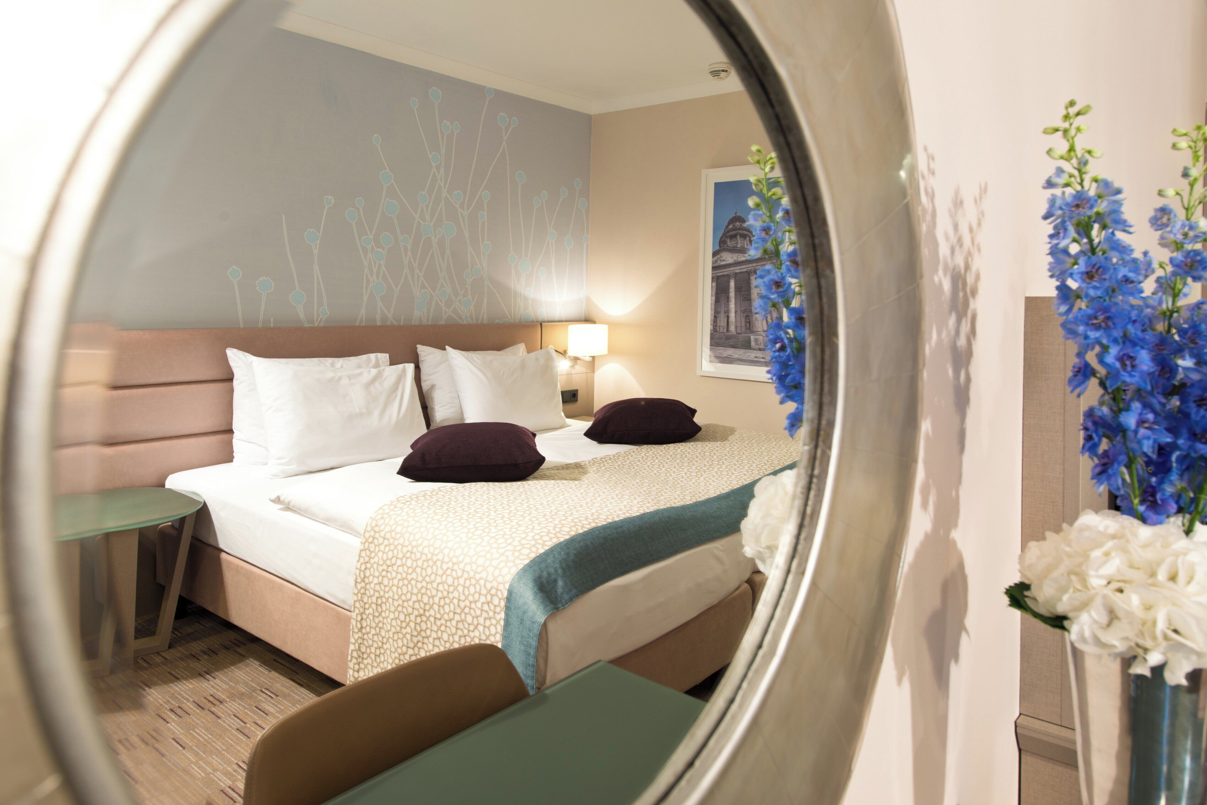 A hotel room with a bed, bedside table, and a mirror reflecting the room.