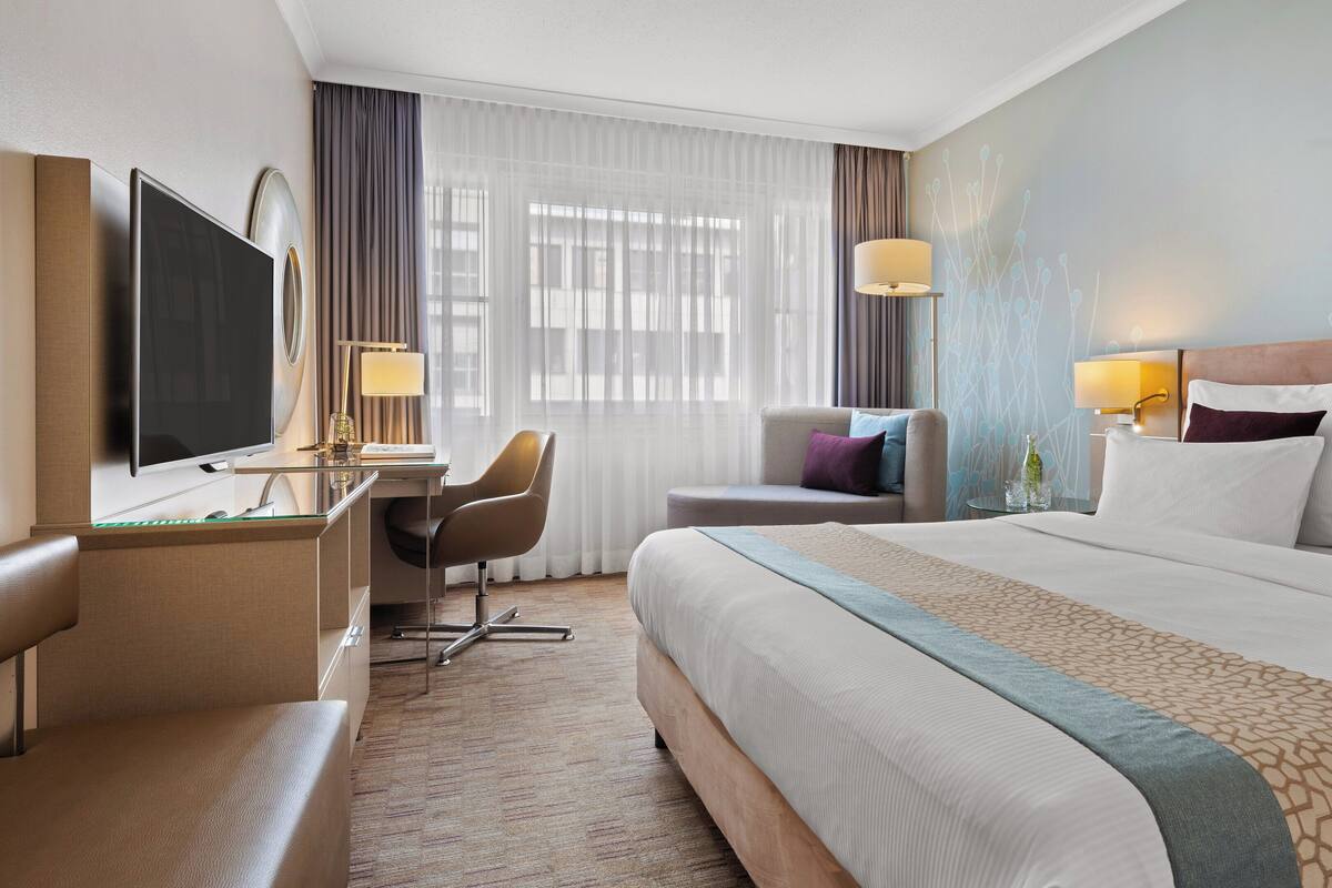 Habitación de hotel con una cama grande, un escritorio con computadora, una silla y un televisor.