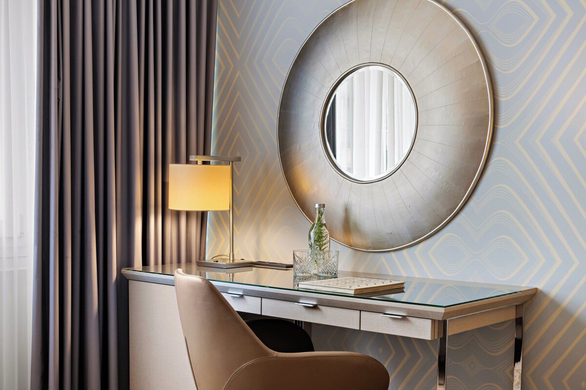 Una habitación de hotel moderna con un escritorio, una lámpara, un espejo y una silla.