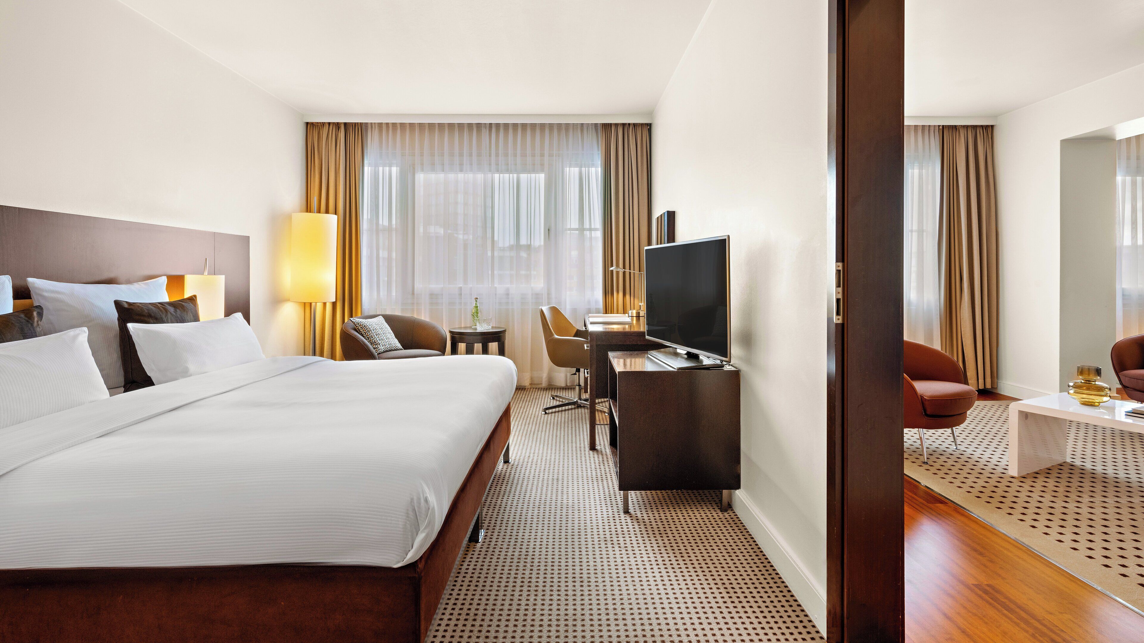 Une chambre d’hôtel avec un grand lit, un bureau avec une télévision, une chaise et une petite table avec une lampe.