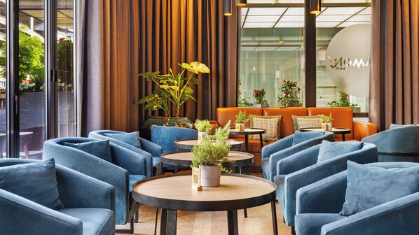 Un área de descanso moderna con sillones azules, una mesa de centro de madera y sofás naranjas.
