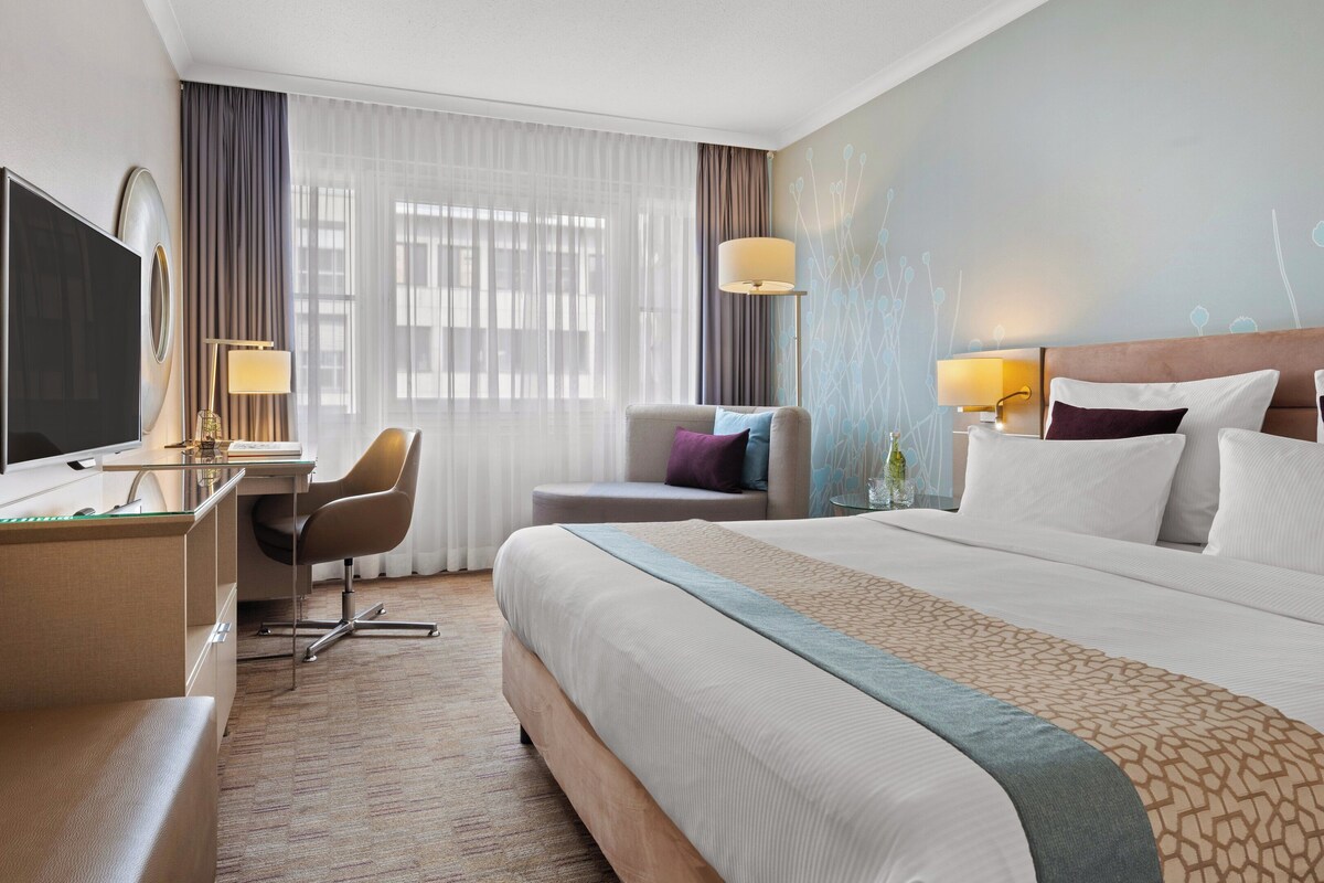 Habitación de hotel con una cama grande, un escritorio con computadora, una silla y un televisor.