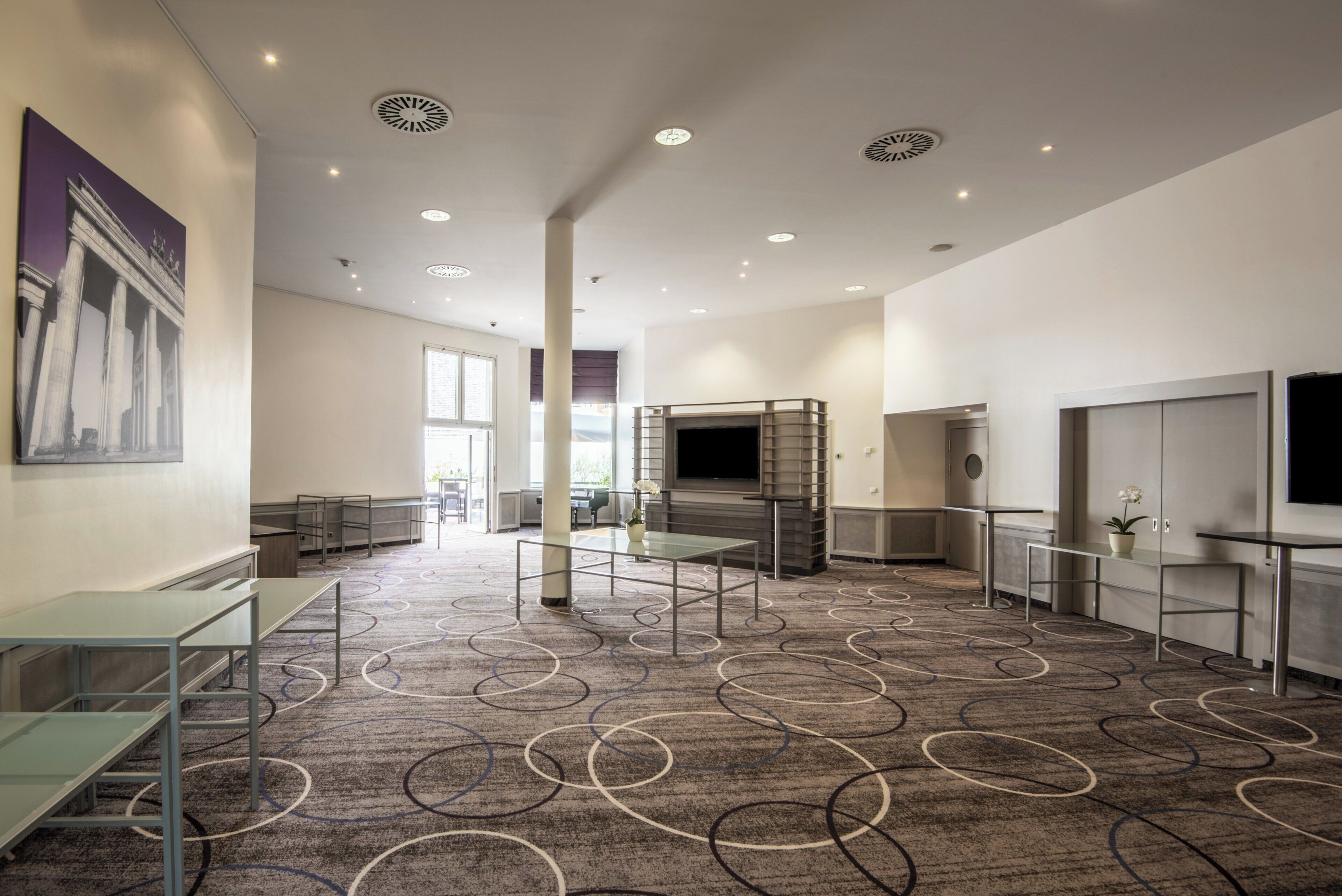 Un hall d’hôtel spacieux, avec un tapis à motifs, un grand tableau accroché au mur et un écran de télévision.