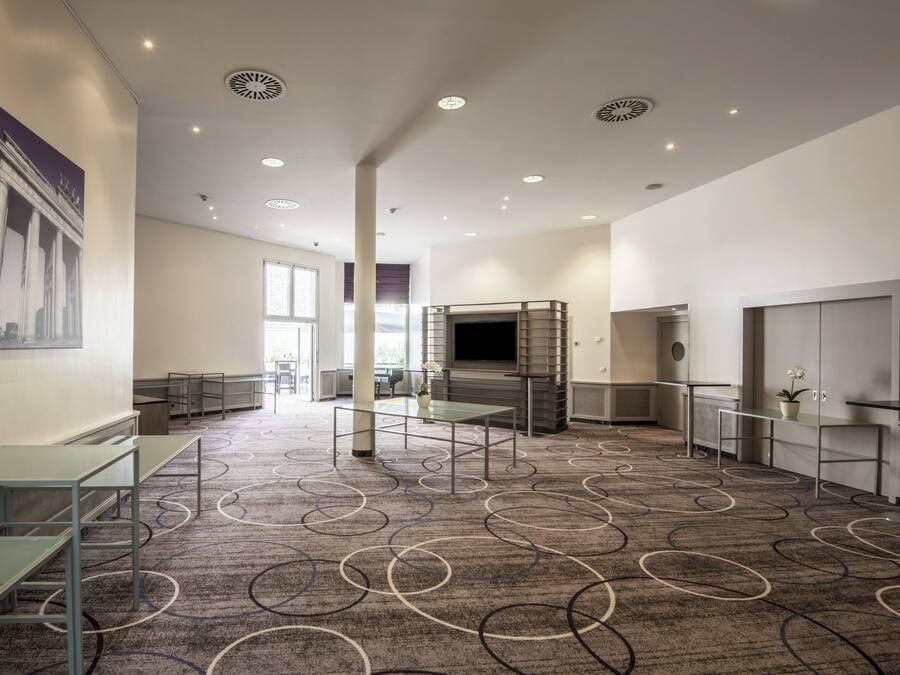 Un hall d’hôtel spacieux, avec un tapis à motifs, un grand tableau accroché au mur et un écran de télévision.