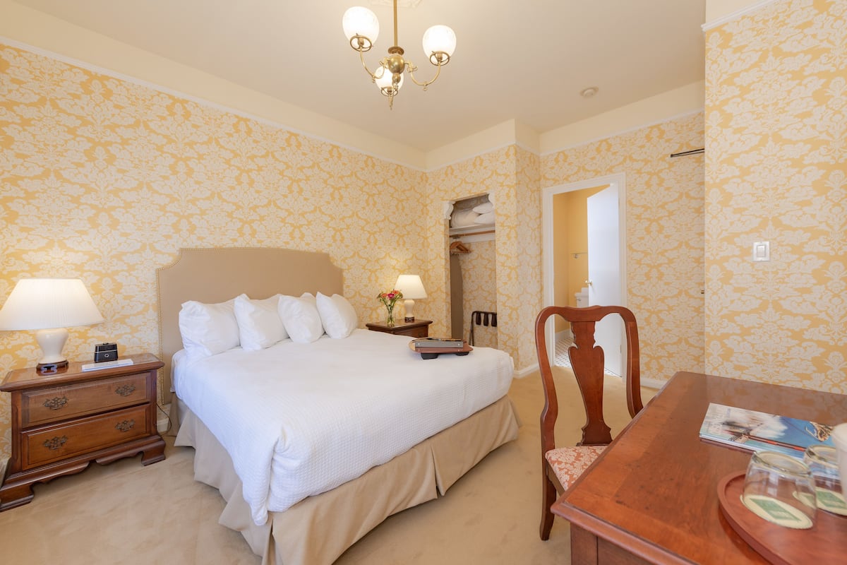 Ein Hotelzimmer mit Bett, Nachttisch, Lampe und einem Holztisch mit Tablett.
