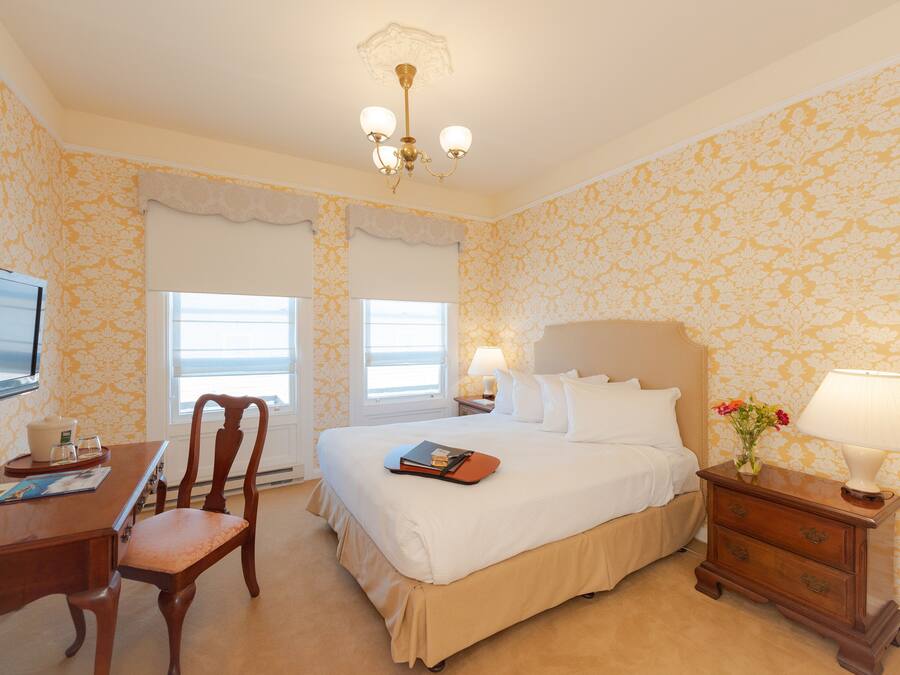 A hotel room with a bed, a desk, a chair, a TV, and a nightstand with a lamp.