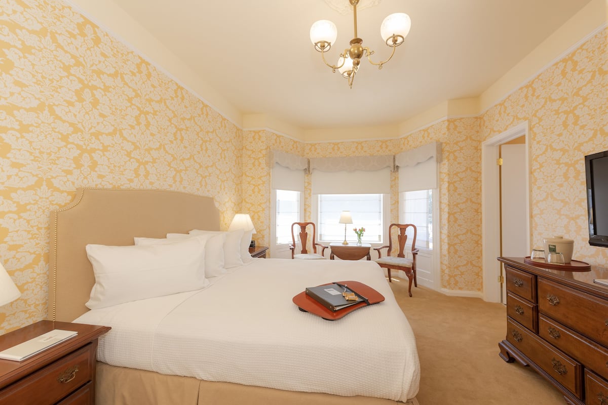 Ein Hotelzimmer mit einem großen Bett, einem Schminktisch, einem Fernseher und einem Fenster mit Vorhängen.