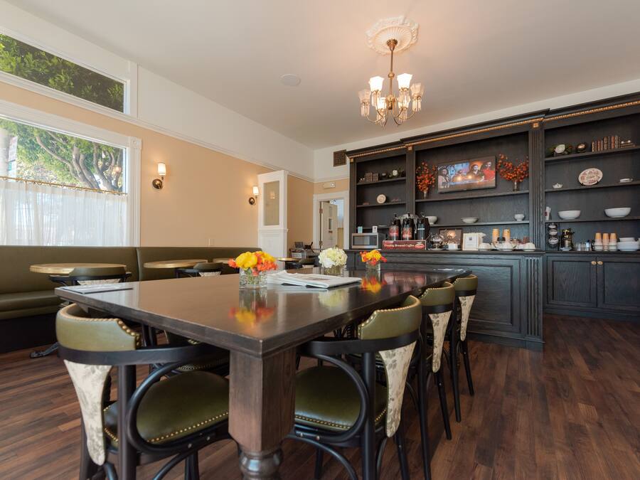 A modern kitchen with dark cabinetry, a central island, and a dining area with green upholstered chairs.