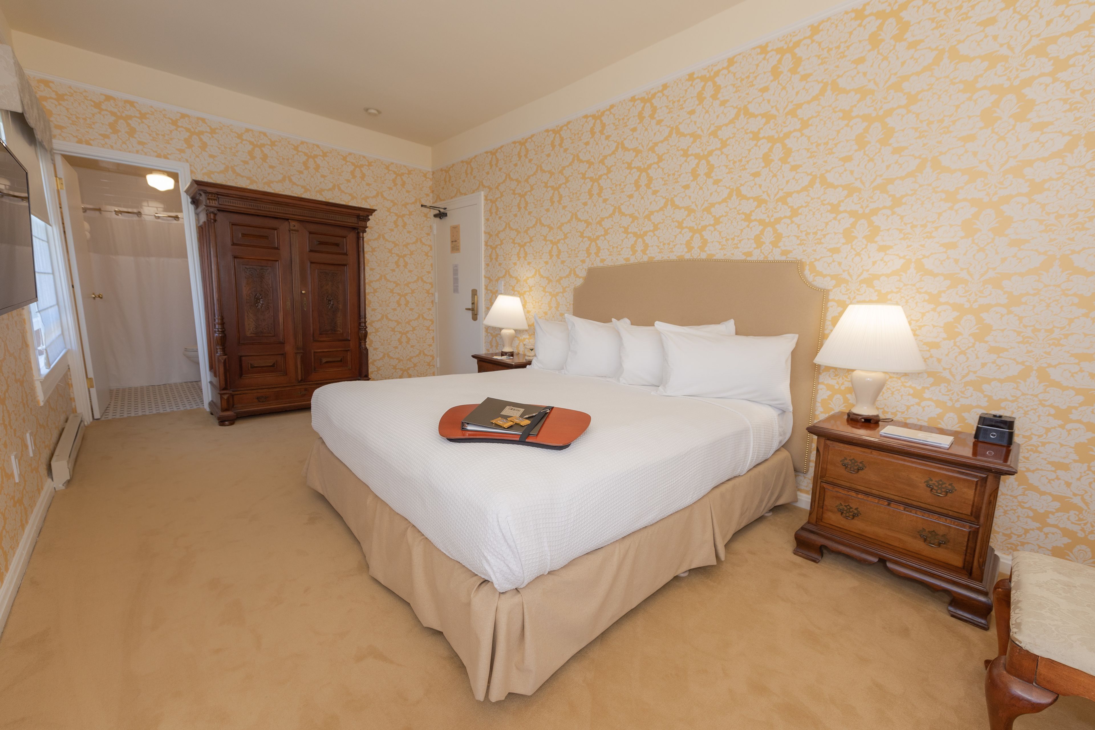 Habitación de hotel con una cama grande, dos mesitas de noche con lámparas, un armario de madera y una puerta que da a un baño.