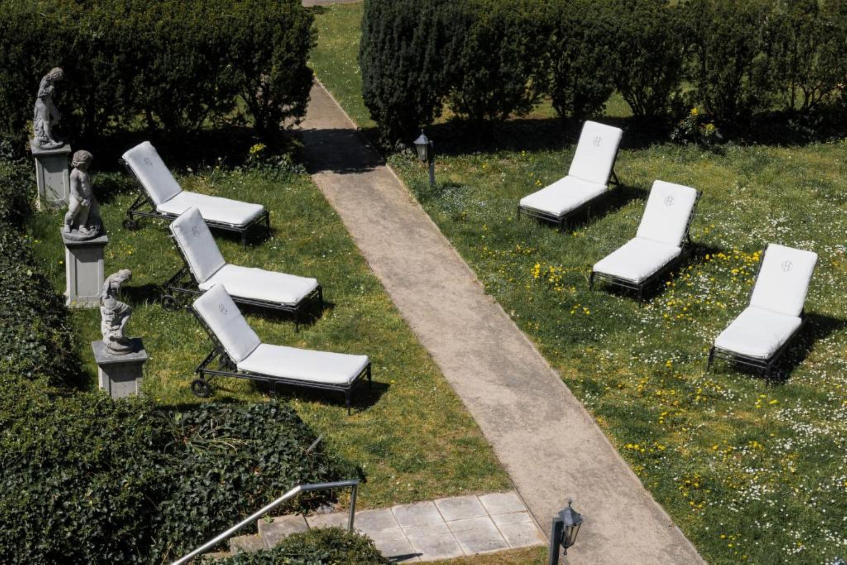 A garden with white lounge chairs arranged in a semi-circle, a paved path, and statues.