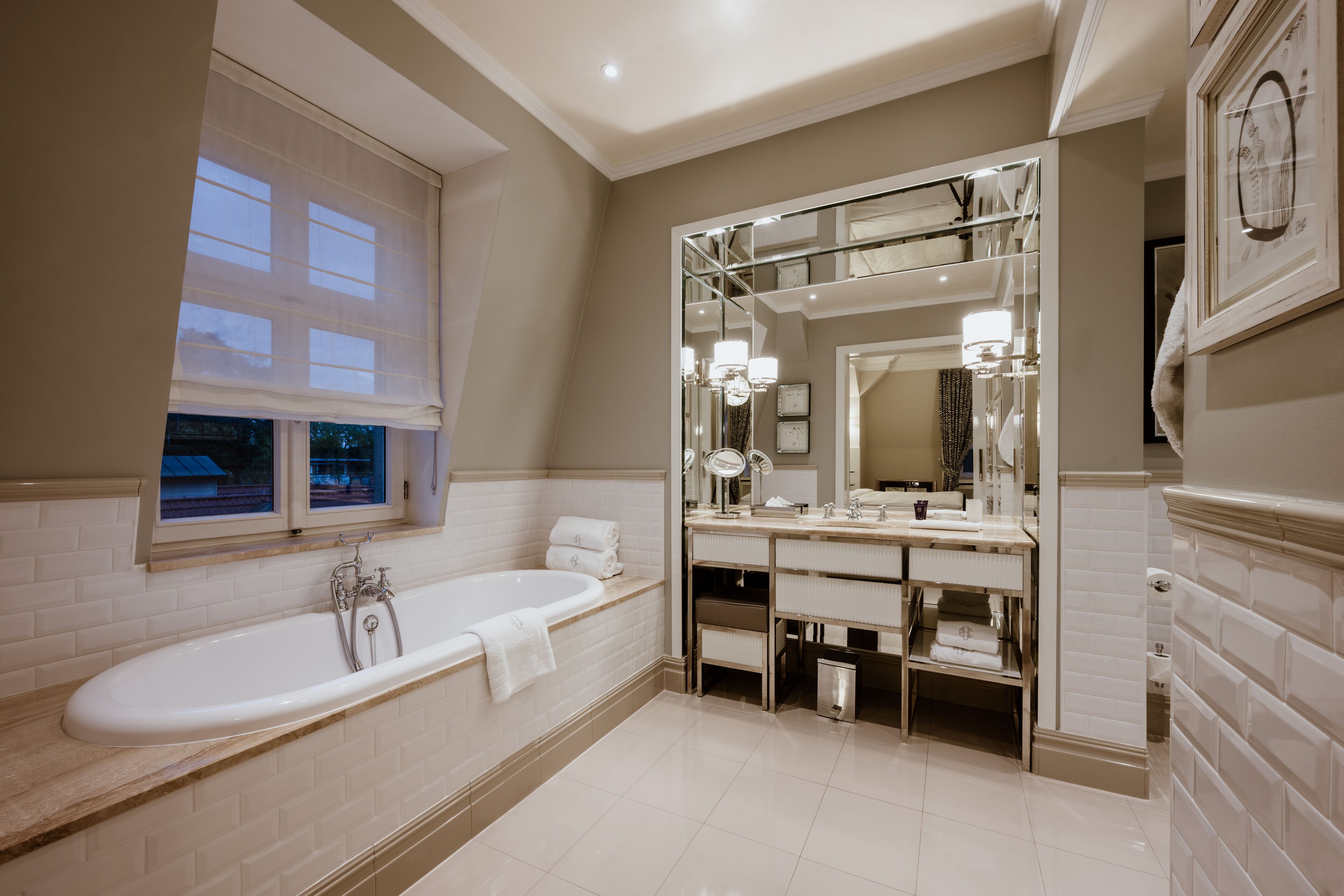 A modern bathroom with a large bathtub, a vanity with a mirror, and a window with blinds.