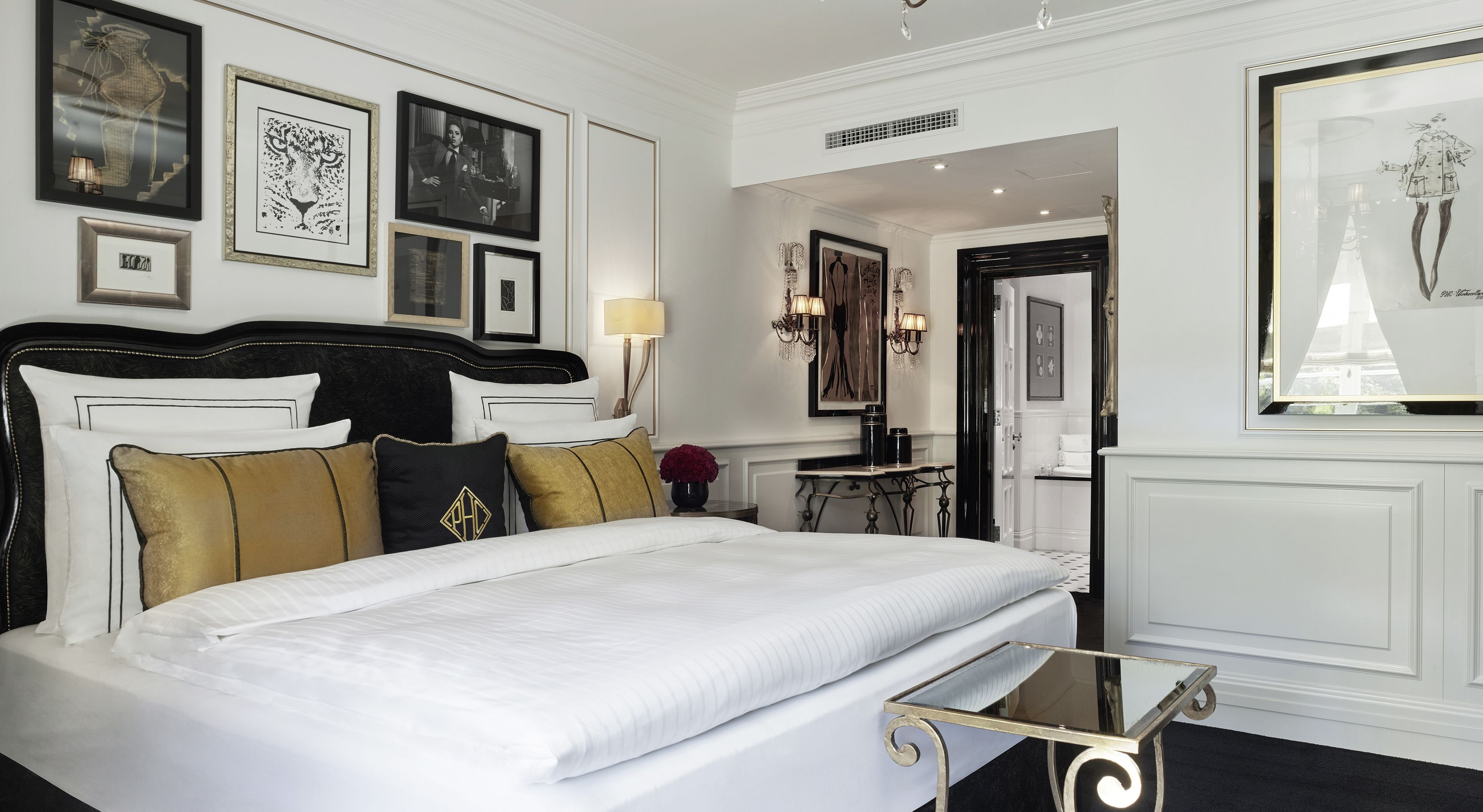 A hotel room with a large bed, a small table, and framed artwork on the walls.
