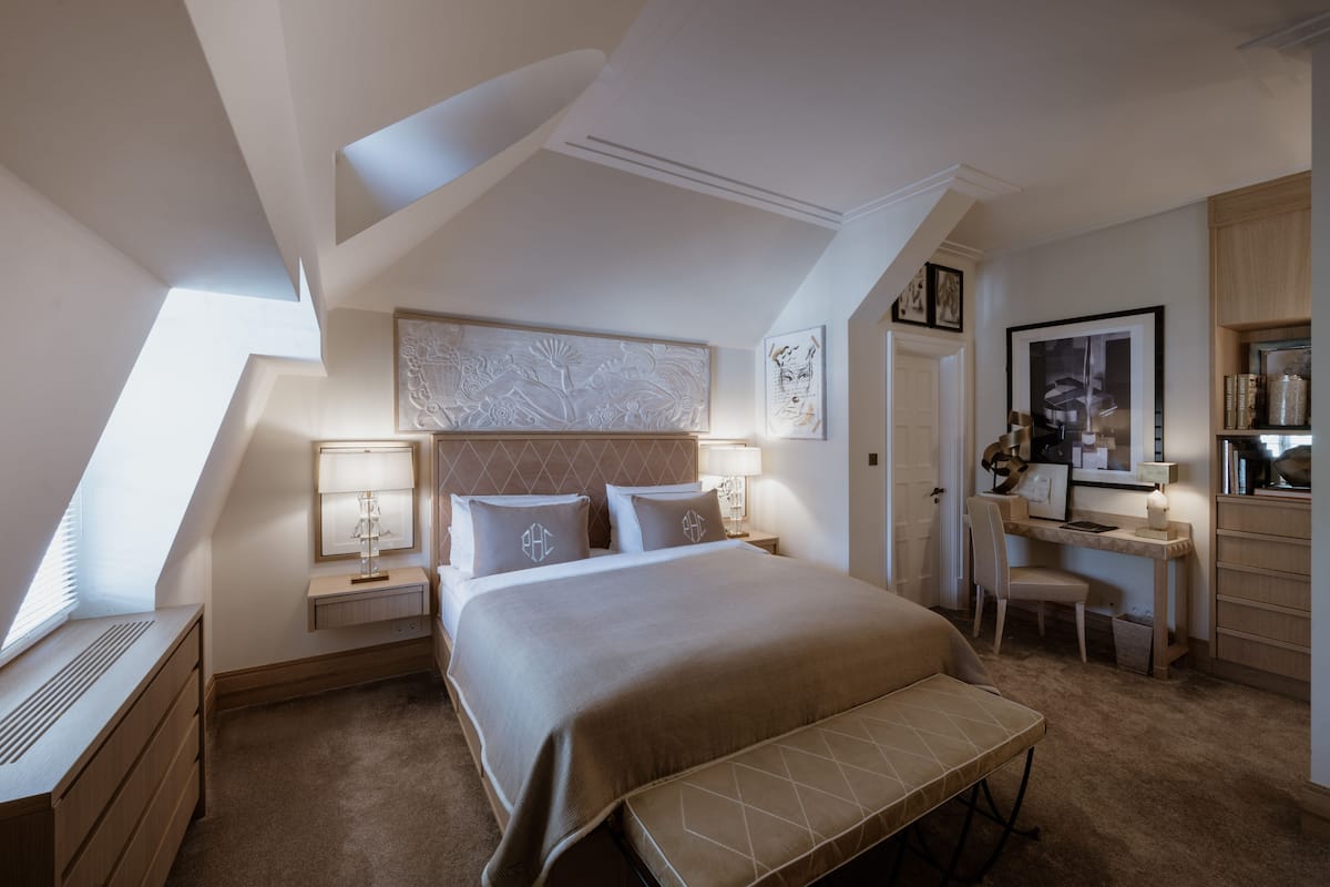 Un dormitorio con una cama grande, un escritorio y una silla. Una ventana proporciona luz natural.