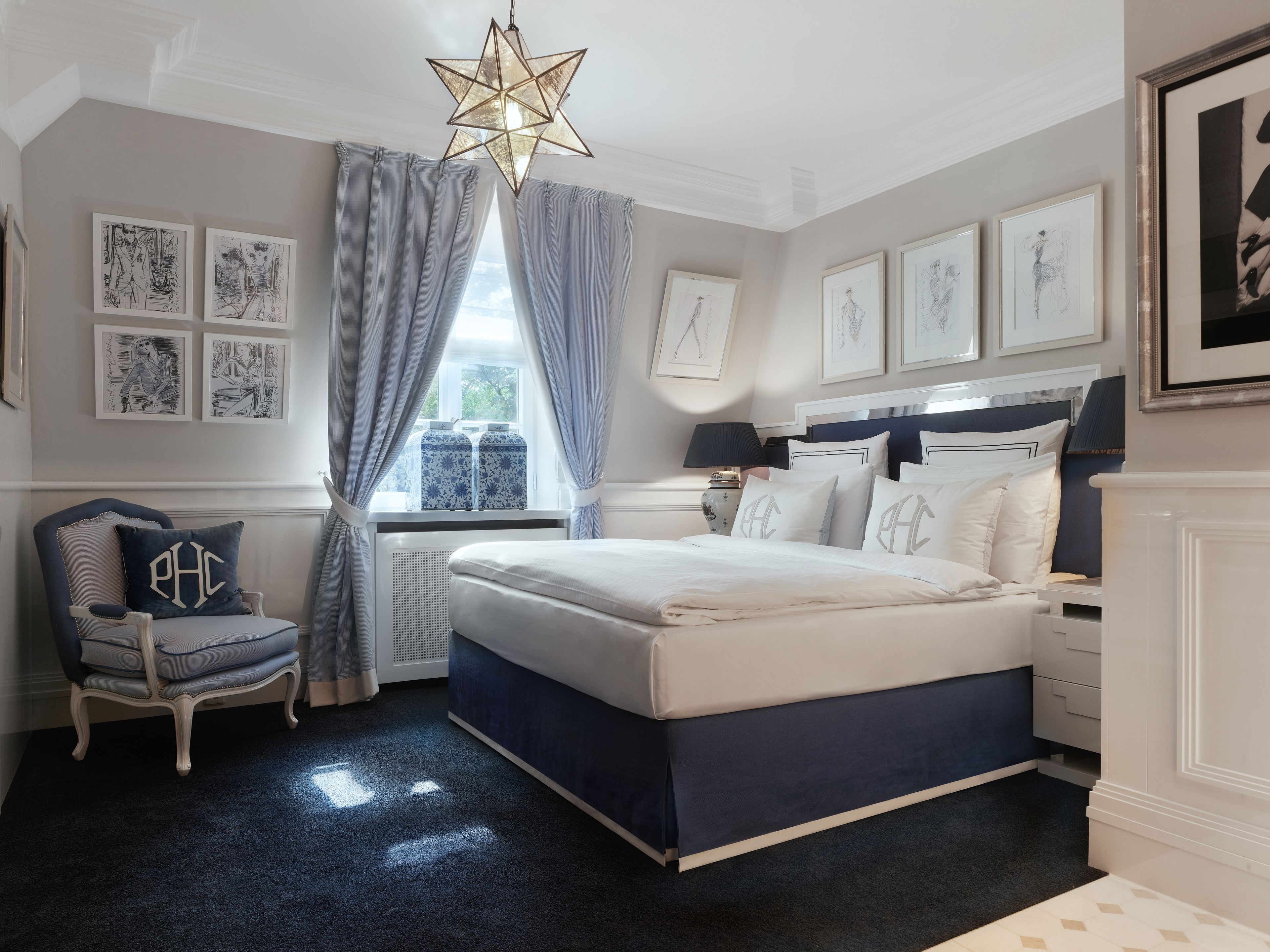 Un dormitorio con una cama grande, una silla con un cojín, una lámpara en forma de estrella y obras de arte en las paredes.