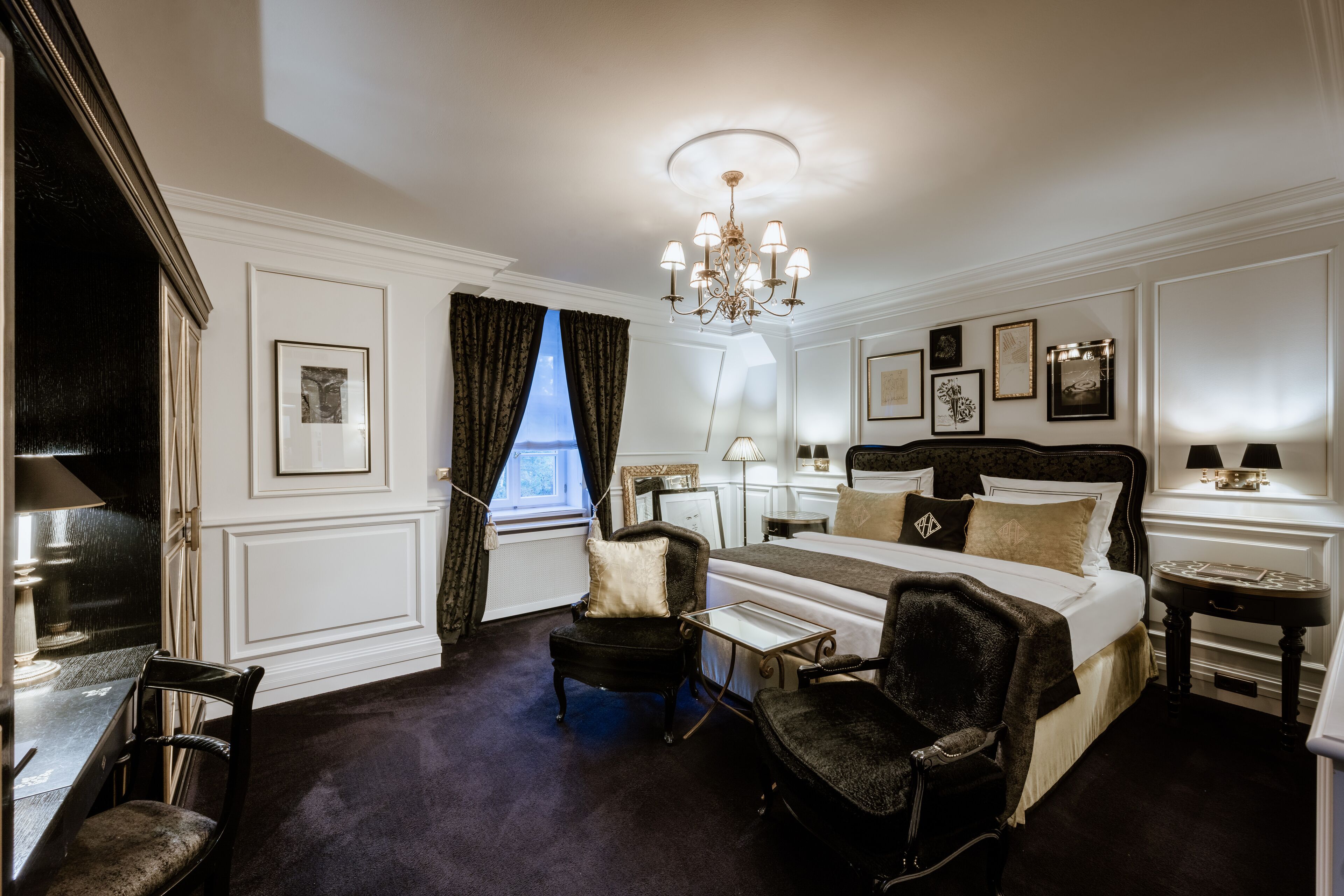 A hotel room with a large bed, two armchairs, a small table, and a chandelier.