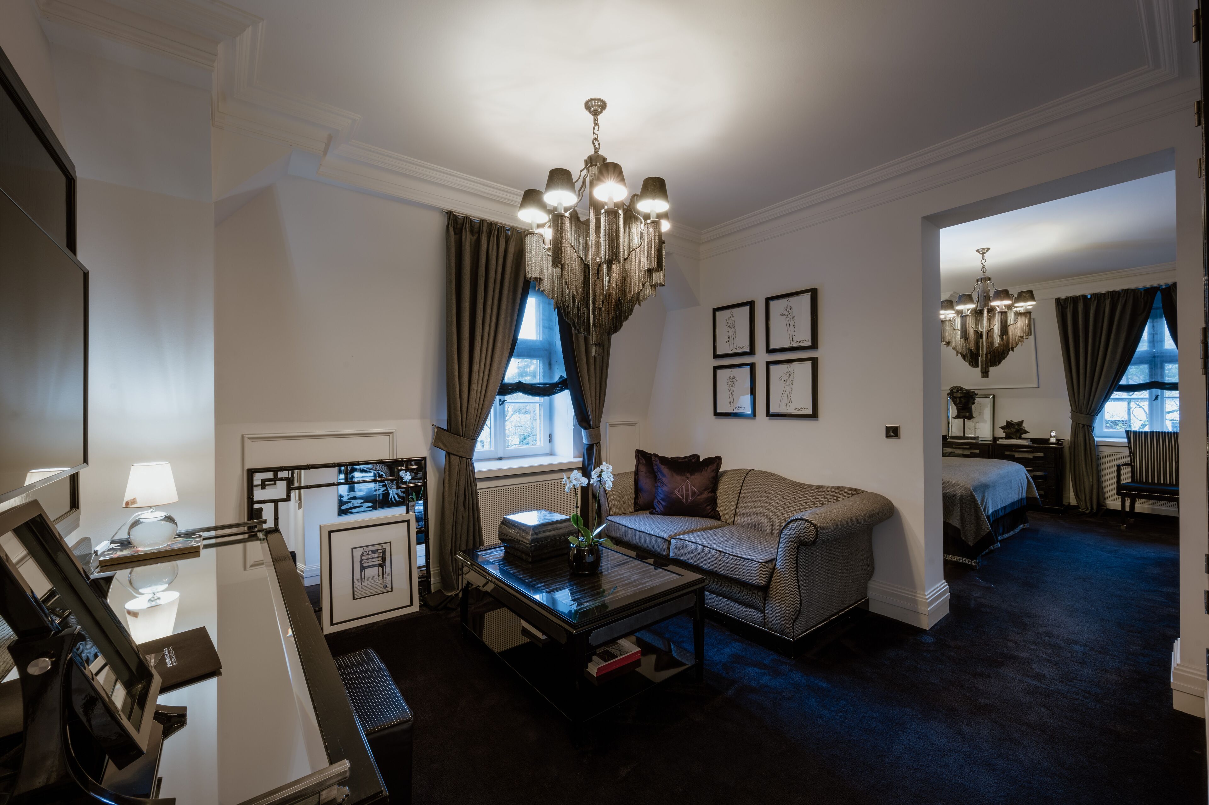 A hotel room with a sofa, a coffee table, a chandelier, and a bed.