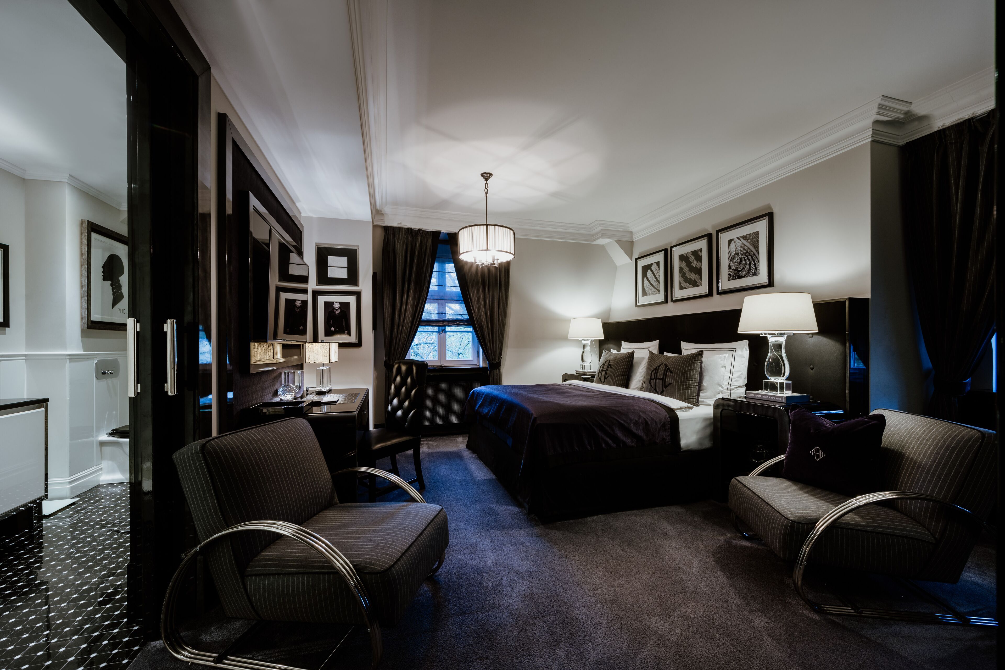 Ein Hotelzimmer mit einem großen Bett, zwei Sesseln, einem Schreibtisch und einem fensterbepflanzten Fenster.