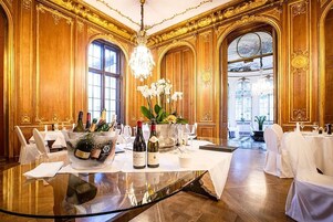 A luxurious dining room with a round glass table, elegant white chairs, and a chandelier.